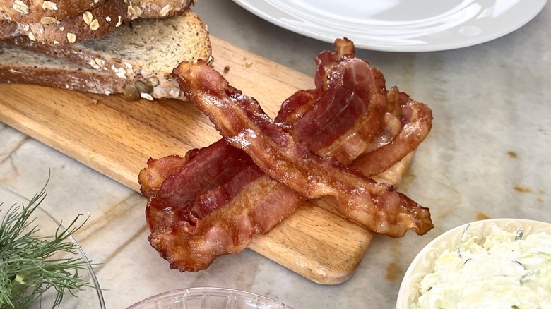 Close up of slices of cooked bacon piled on top of one another on a wooden cutting board