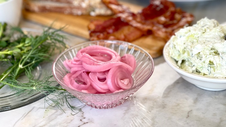 Close up of pickled onions in a glass bowl next to sprigs of dill