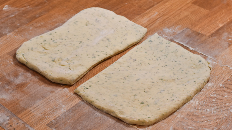 flat bread dough cut in half on wood board