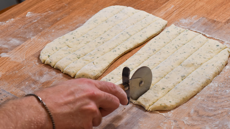 cutting breadstick dough in strips with pizza cutter