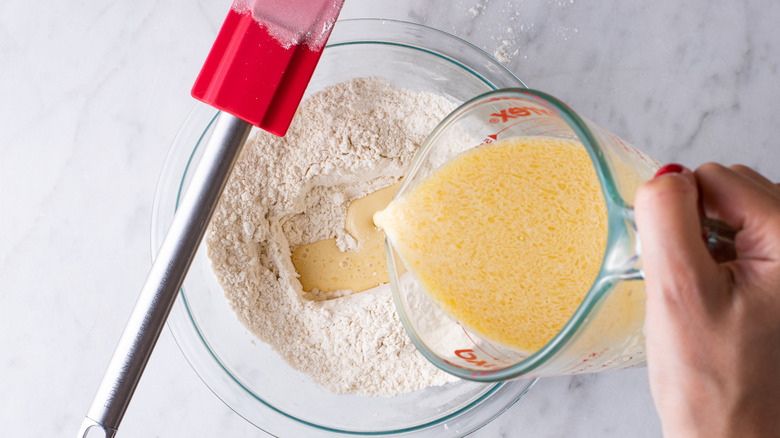 Hand pouring milk mixture into flour.