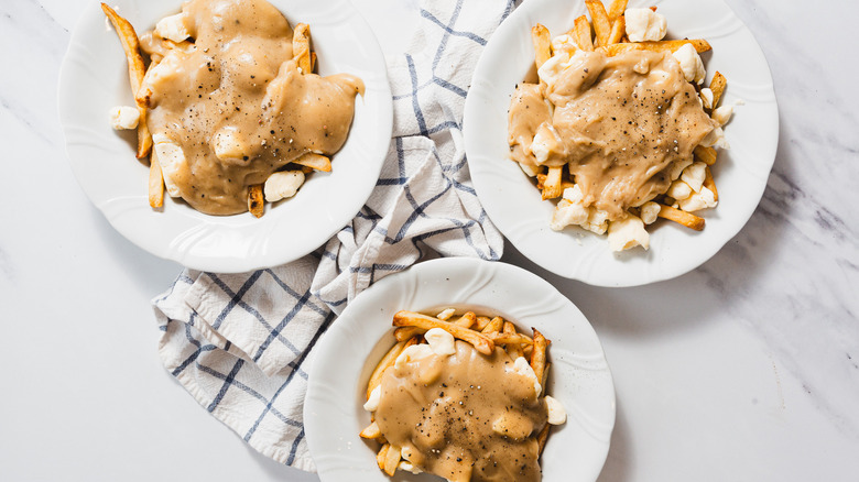 Three plates of poutine with a napkin