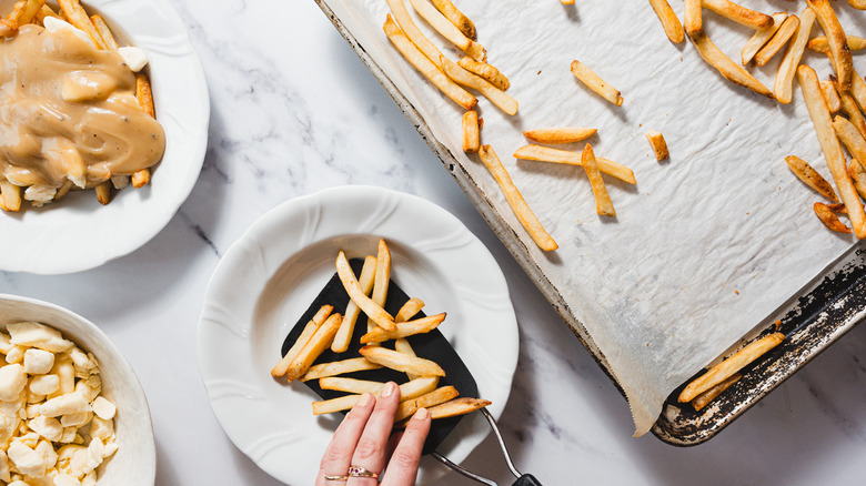 Adding fries to a plate surrounded by fries on baking sheet and curds