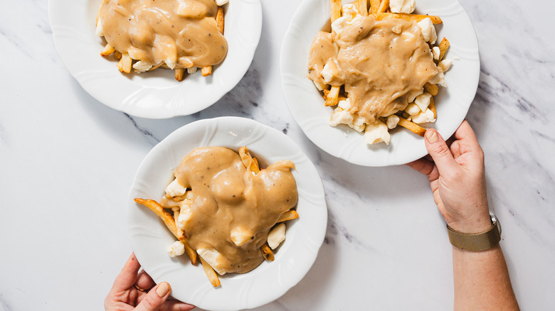 Person serving three plates of poutine with a napkin