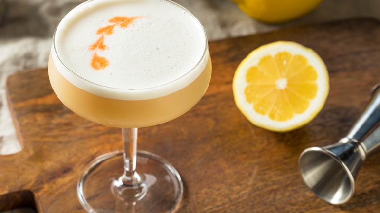 A Pisco Sour cocktail with a jigger and orange