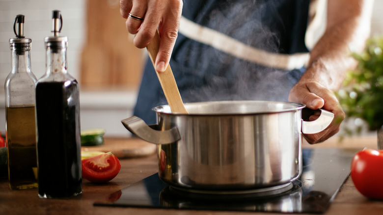 Hands stir wooden spoon in pot