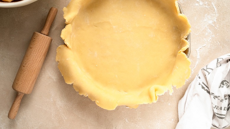 Uneven pie dough in a pan beside a rolling pin