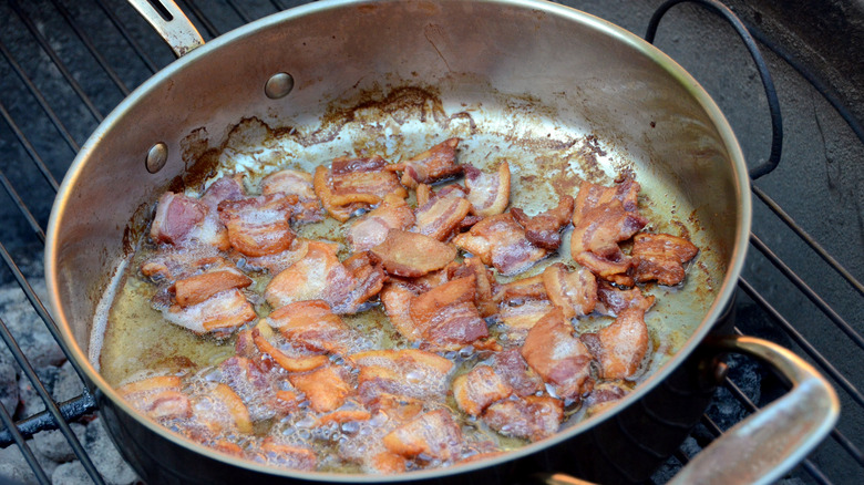 bacon bits frying in grease in a metal pan