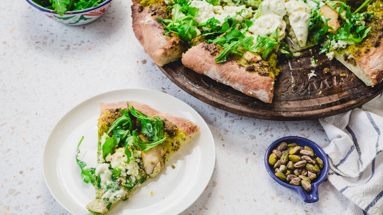 Pizza with a slice on a plate besides pistachios