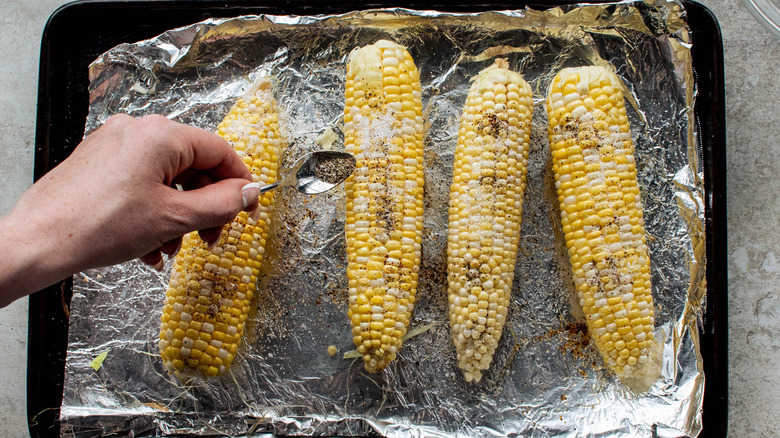 hand sprinkling seasoning onto corn