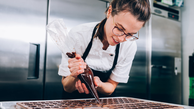 A smiling chocolatier holding a frosting bag and working in a kitchen 