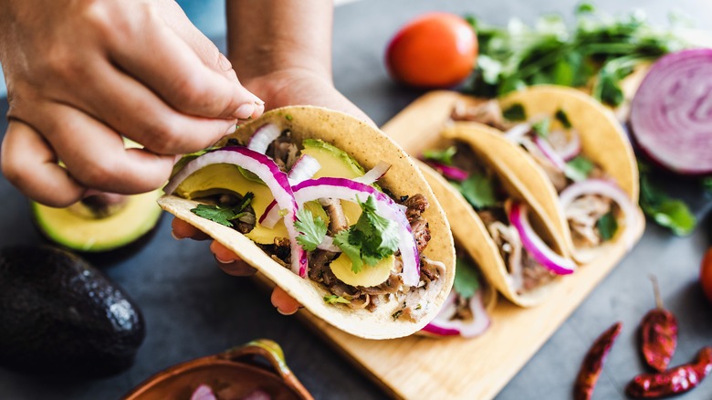 hands holding taco with more tacos on table