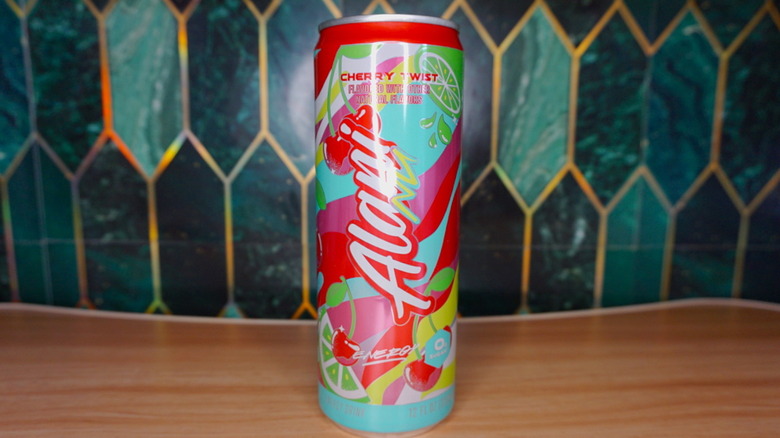 Cherry Twist Alani Nu energy drink on a wooden table, against a green-and-gold tiled background