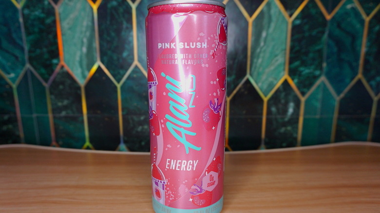 Pink Slush Alani Nu energy drink on a wooden table, against a green-and-gold tiled background