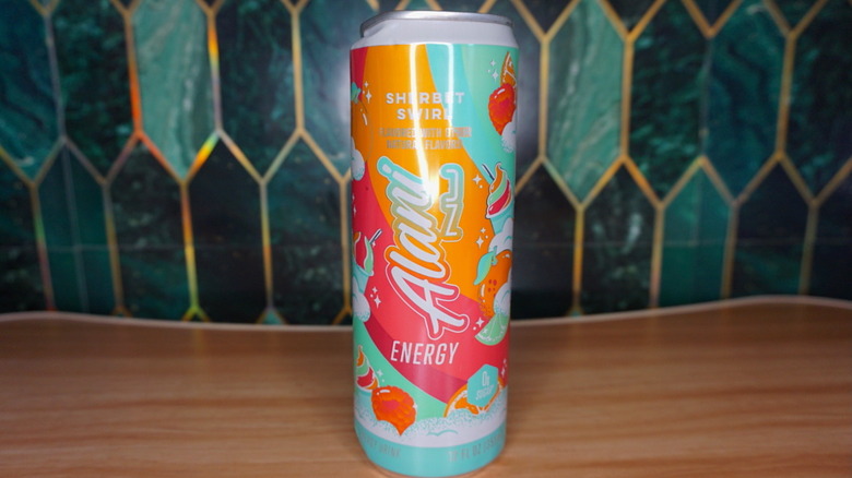Sherbet Swirl Alani Nu energy drink on a wooden table, against a green-and-gold tiled background