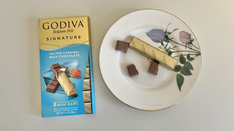 A Godiva salted caramel milk chocolate bar is shown on a plate next to its packaging.