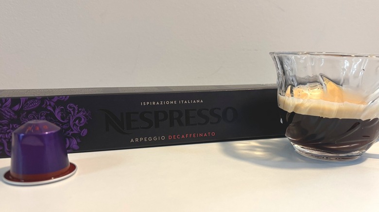 Clear teacup of Nespresso Arpeggio Decaffeinato next to box and pod on white table