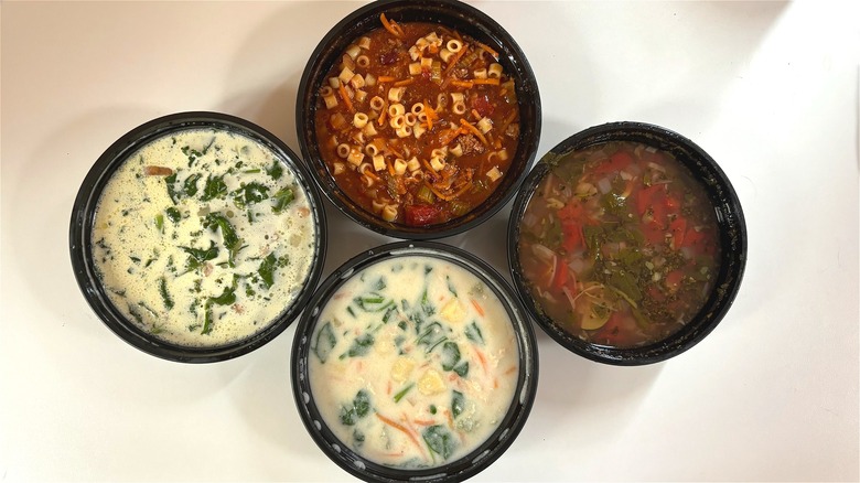 Four Olive Garden soups in black takeout containers on table