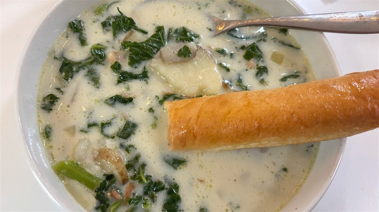 Breadstick dipped in bowl of Zuppa Toscana on table