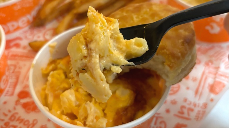 Black fork holding Popeyes mac and cheese with biscuit in the background