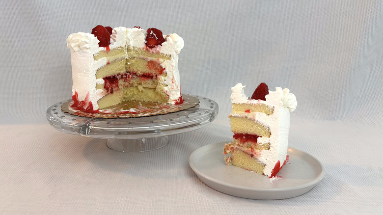 Publix strawberry & cream supreme cake on glass cake stand and slice on white plate with white background