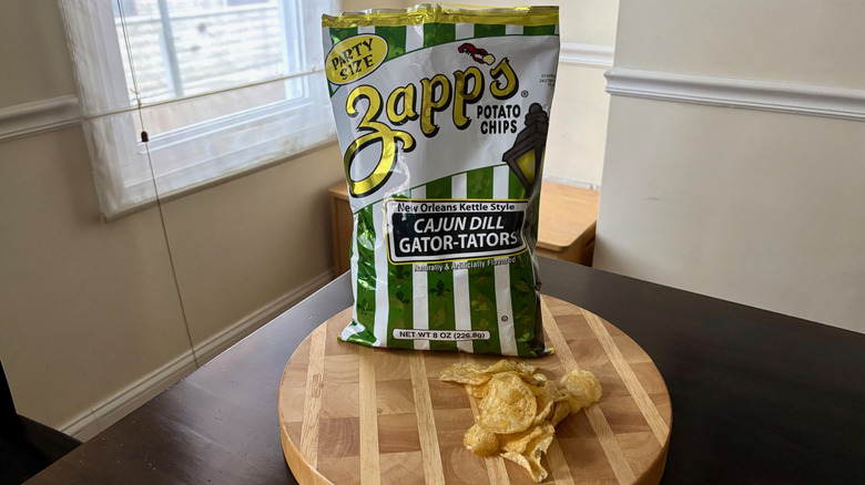 Bag Zapps Cajun Dill Gator-Tators on a board with handful chips