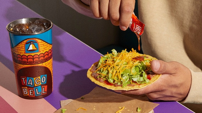 Person drips Taco Bell fire sauce onto a tostada from decades menu.