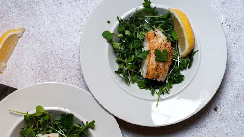 White fish over a bed of greens with yellow lemon