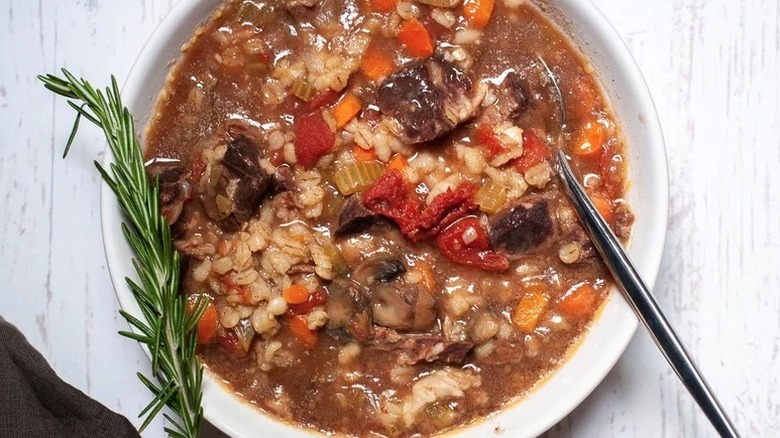 Bowl of red beef and barley soup with a green sprig