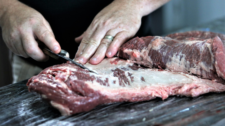 Close up of a beef brisket being trimmed of its fat