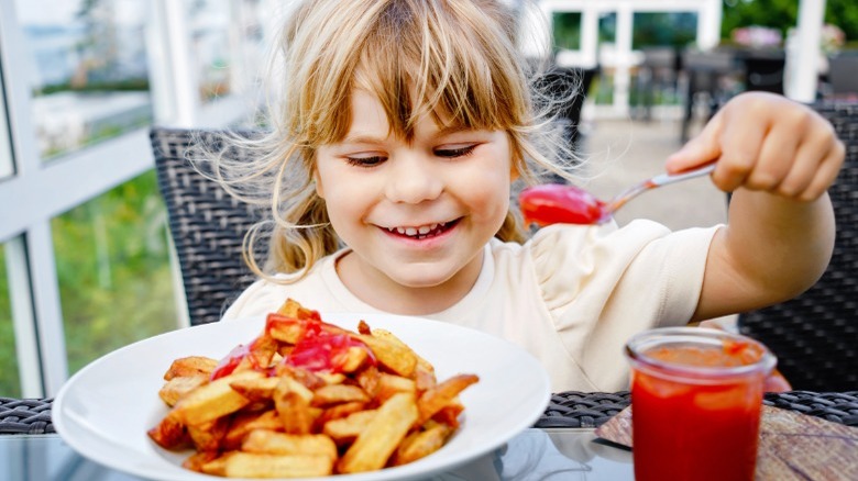 Little girl putting ketchup on fries