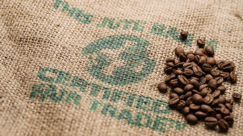 Coffee beans are piled on top of a burlap sack stamped with "Certified Fair Trade."