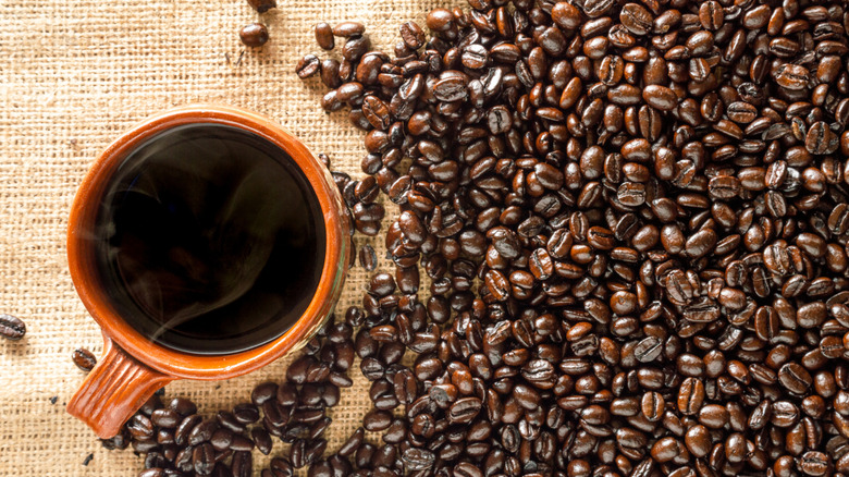 A mug of coffee sits next to a pile of coffee beans.