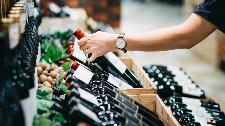 person reaching for bottle of red wine in shop