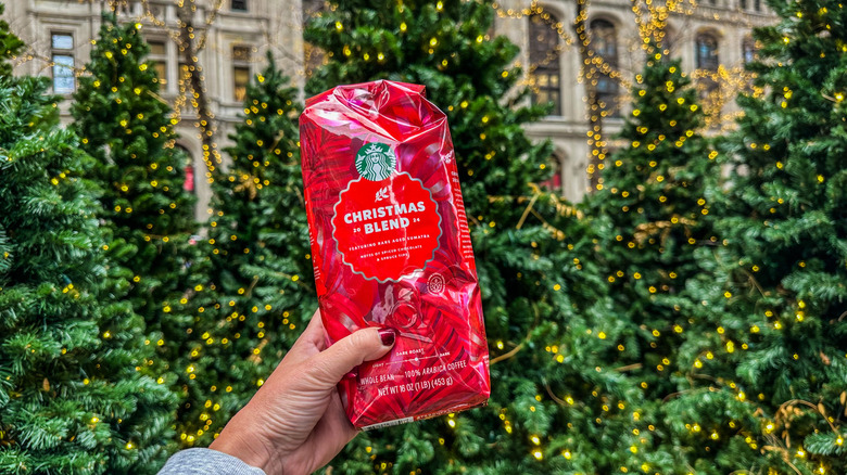 Starbucks Christmas Blend held up in front of Christmas trees