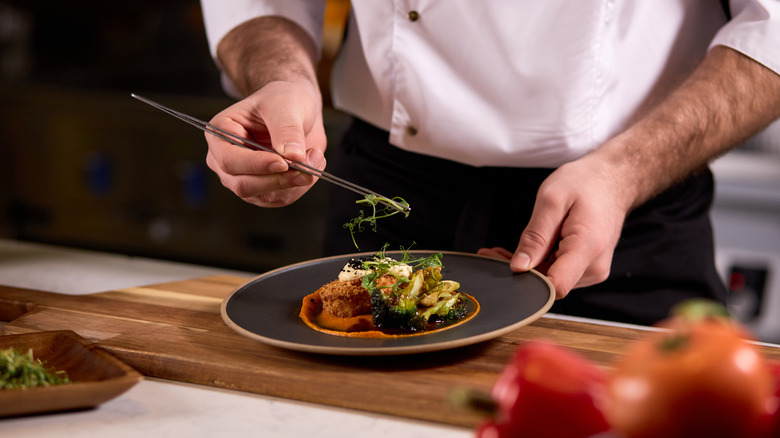 Chef tweezing greens on plate