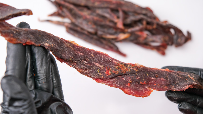 person making jerky meat wearing black gloves