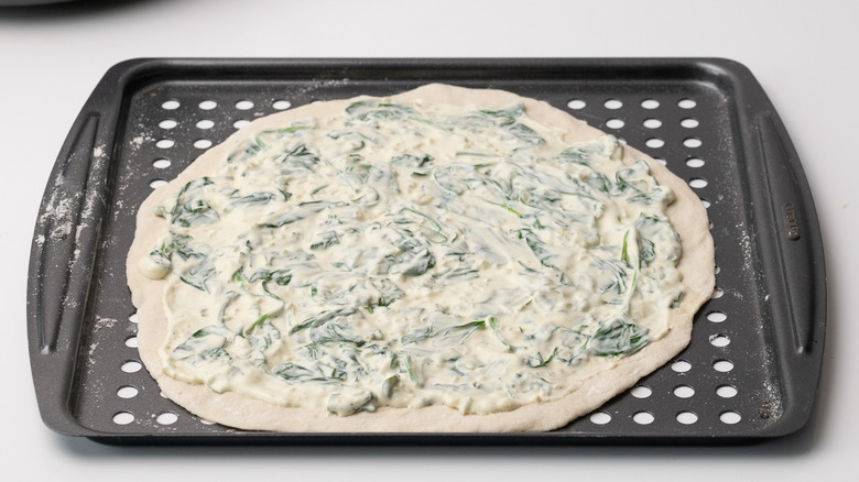 assembling cheesy spinach artichoke pizza