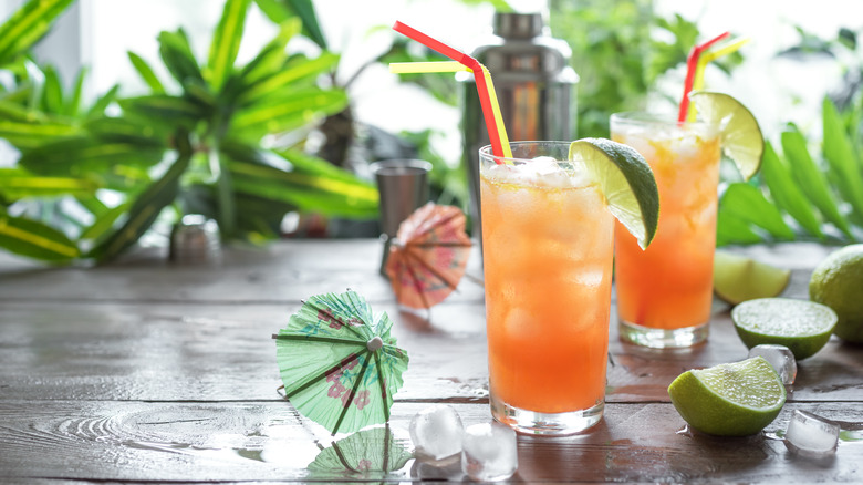 Two Zombie cocktails on a table next to paper umbrellas and limes