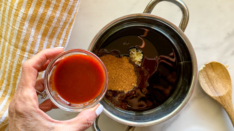 adding sriracha to pot of sauce ingredients