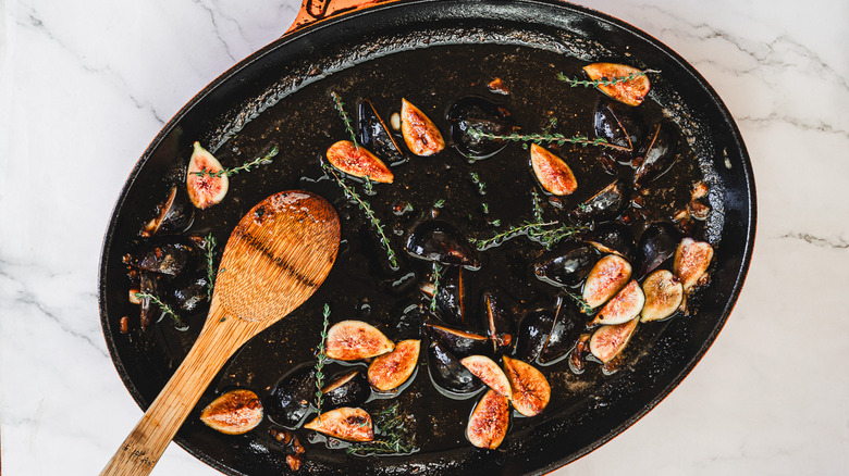 A hand stirring figs and thyme in a pan