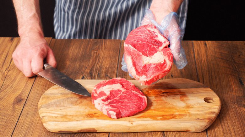 A butcher holding up a slice of raw prime rib while another slice sit on a cutting board