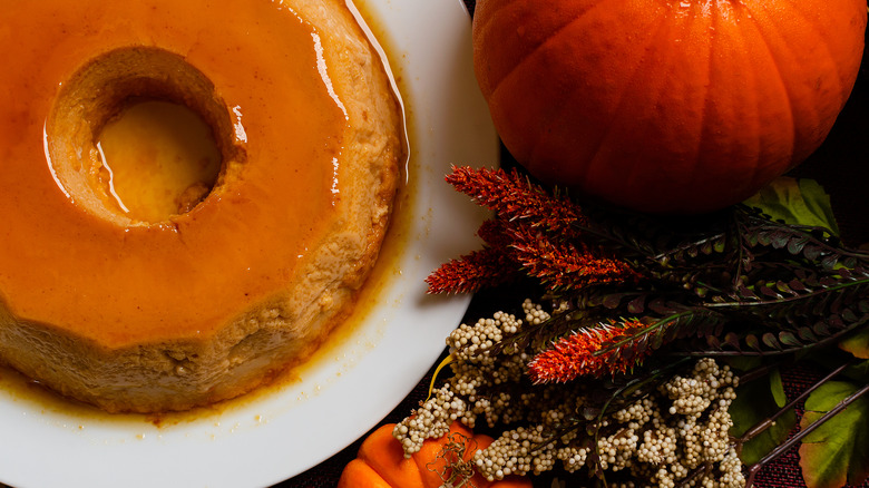 A plate of flan next to a pumpkin and plants