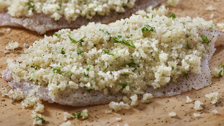 A raw chicken cutlet with breadcrumbs and spices on top