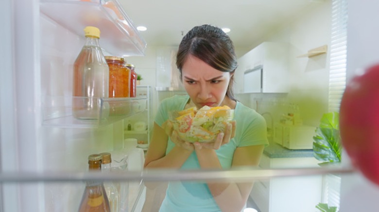 A woman smelling a salad in the refrigerator