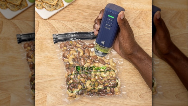 Person using the handheld FoodSaver device to vacuum seal mixed nuts