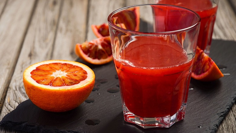 Sliced blood oranges next to a glass of red juice