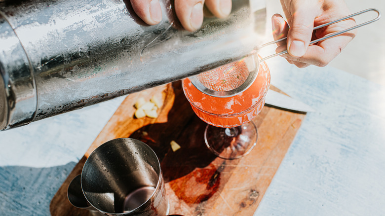 Hands pouring cocktail into glass