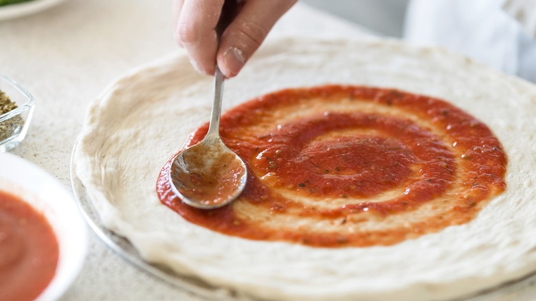 spoon spreading sauce over pizza dough