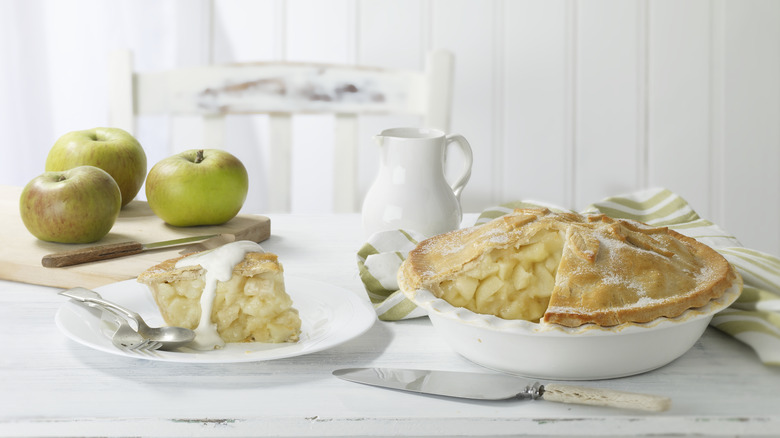 Apple pie on table with fresh apples